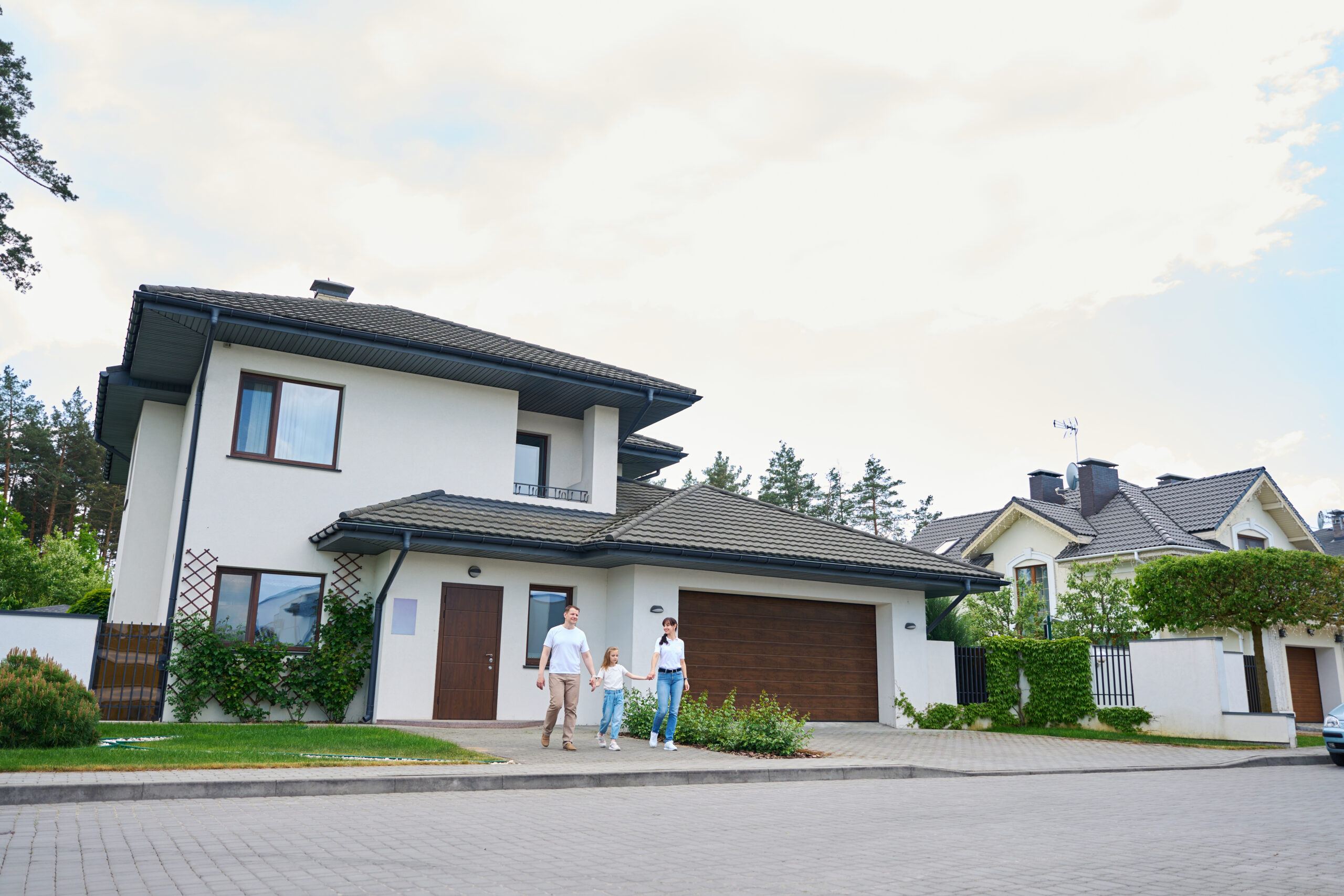 Smiling caucasian mother, father and daughter holding hands and going from new modern townhouse outdoors in warm cloudy day. Family future planning, relationship and spending time together