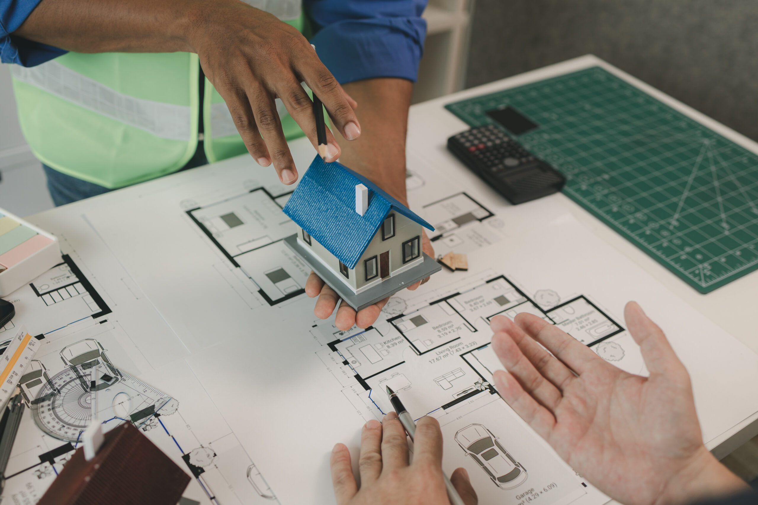 two architect is in office and sharing their strategy idea of building plan to each other, there are blueprint and house model on the desk in the office with two engineers, meeting